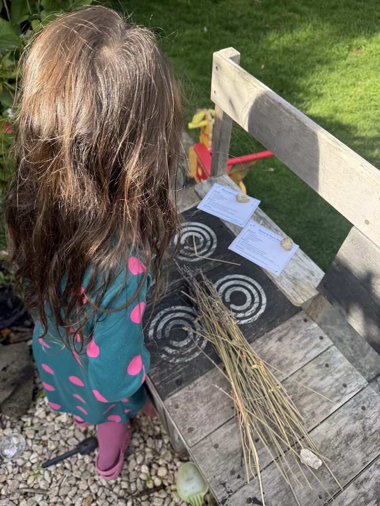 child reading A Crafty Day potion card to make a magical potion at her mud kitchen